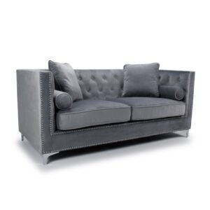 Gray velvet sofa with tufted back, two square pillows, and cylindrical side cushions. Silver studs accent the arms and base, on a white background.