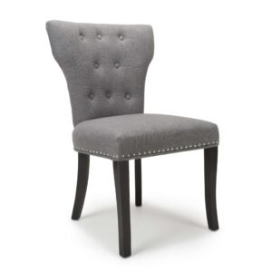 A modern gray upholstered chair with a tufted backrest, silver nailhead trim, and dark wooden legs. The design is elegant and contemporary.